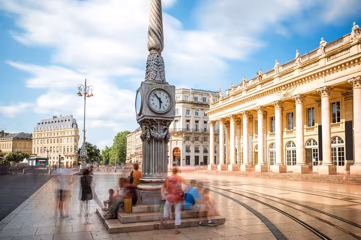 Clock tower at Place de la Comédie in Bordeaux Old Town with Grand Théâtre colonnade and blurred pedestrians