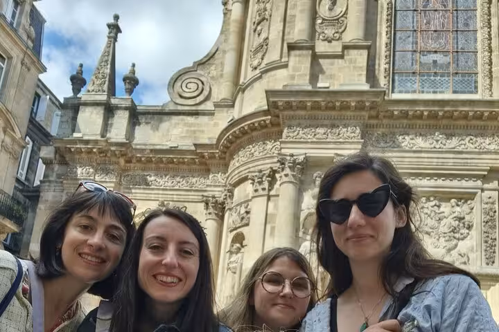 Four women smiling in front of ornate Baroque church facade in Bordeaux Old Town