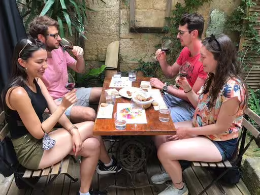 Grupo pequeño en Burdeos degustando vinos tintos y quesos en patio histórico durante tour enológico
