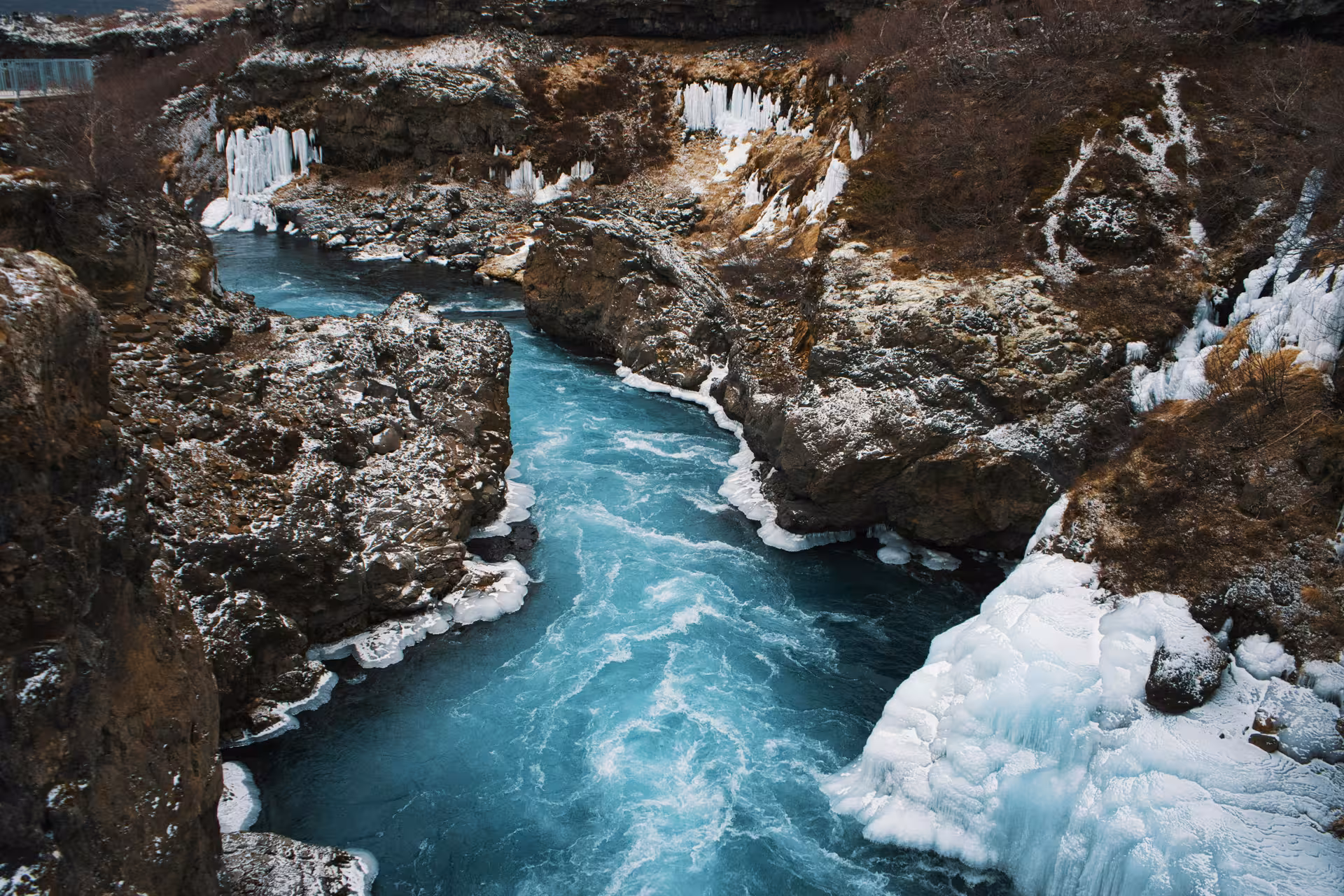 Turquoise glacial river flowing through snow-covered rocky canyon with ice formations in Borgarfjordur, Iceland