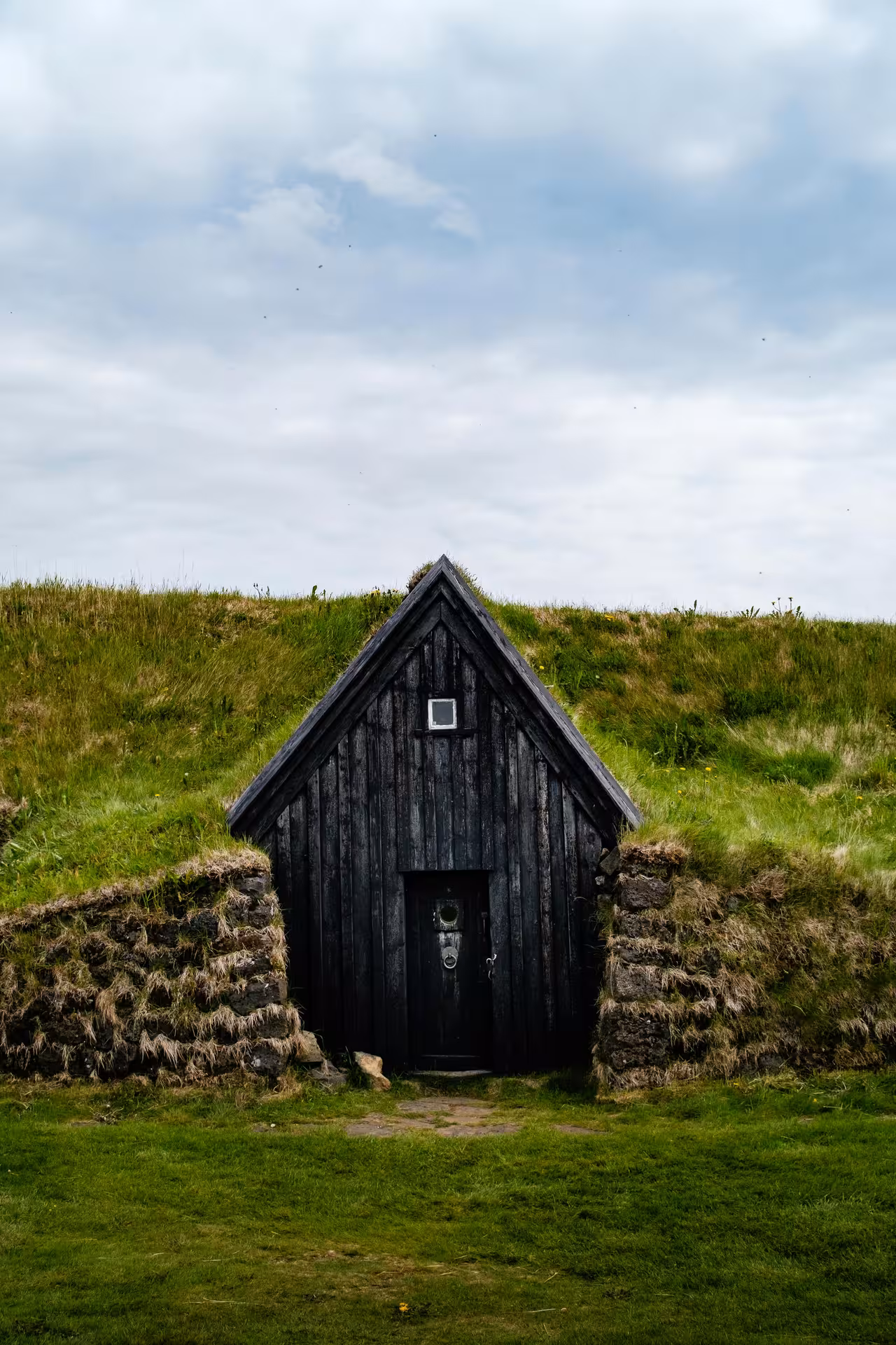 Traditional Icelandic turf house with dark wooden facade built into a grass-covered hillside in West Iceland