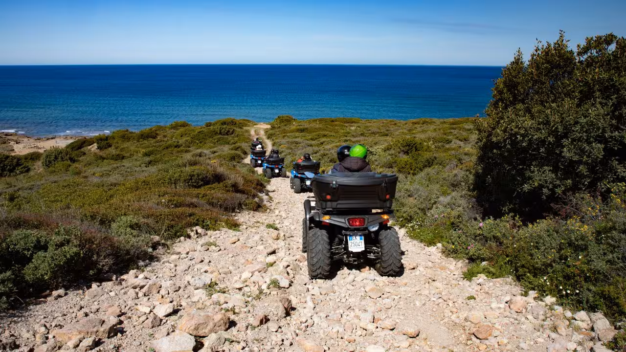 Group enjoying an exhilarating Bosa ATV ride along a rugged coastal path with stunning sea views.