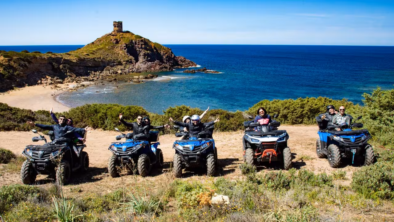 Group enjoying an ATV ride along Bosa's stunning coastline with a view of a historic tower and clear blue sea.