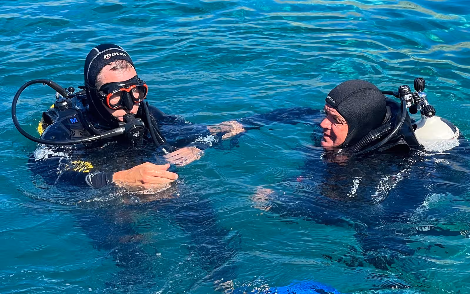Two divers communicate underwater in Bosa, Sardinia, showcasing teamwork and safety during a diving baptism experience.