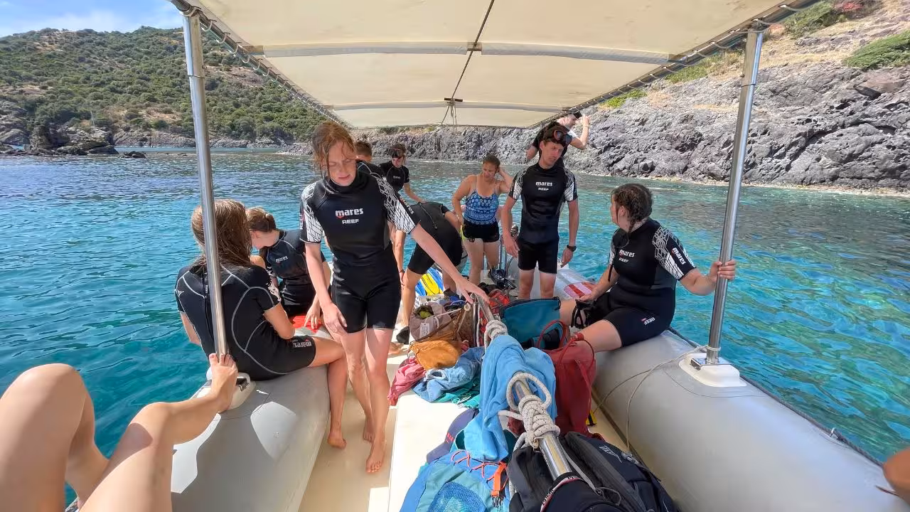 Group of snorkelers in wetsuits preparing on a boat near Capo Marrargiu's scenic coastline during a Bosa tour.