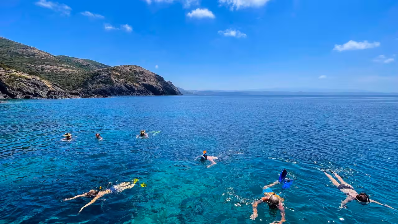 Group snorkeling in the vibrant blue waters of Capo Marrargiu, with scenic cliffs in the background.
