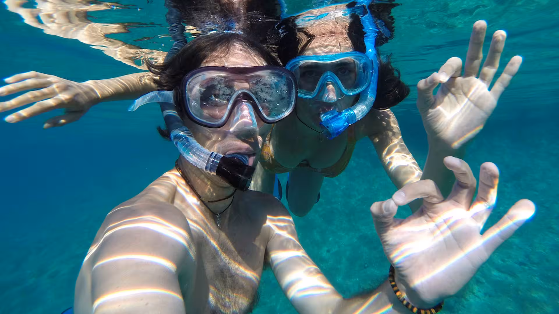 Two snorkelers giving an OK sign underwater in the crystal-clear waters of Capo Marrargiu, Bosa snorkelling tour.