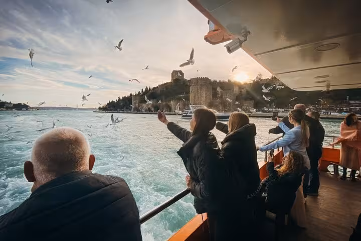 Guests enjoy Bosphorus dinner cruise with private table, feeding seagulls at sunset near Istanbul skyline