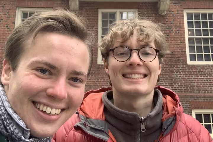 Two smiling visitors taking a selfie in front of a historic red brick building on the Boston Freedom Trail