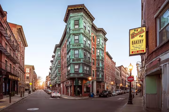 Historic North End Boston street corner with green copper bay windows building and Bova's Bakery sign at sunset