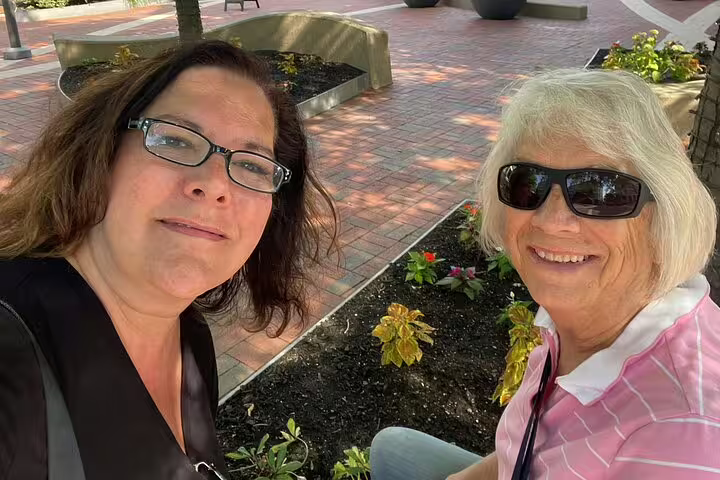 Two women smiling at camera in a brick plaza with garden beds and benches in Boston