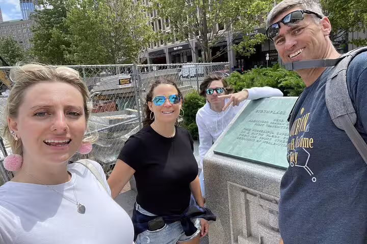 Group of four tourists smiling at historic Boston landmark plaque during self-guided walking tour