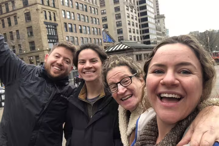 Four smiling friends posing for a selfie on a Boston city street with historic buildings in the background