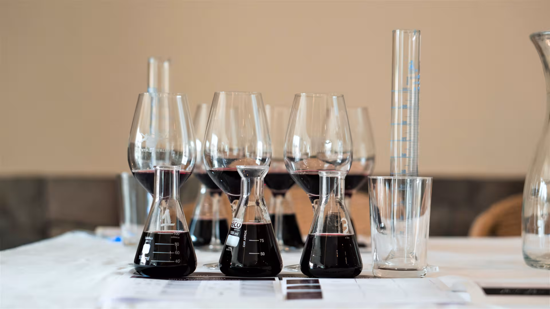 Bottle blending workshop setup with red wine in laboratory flasks, wine glasses, and measuring cylinders on a table