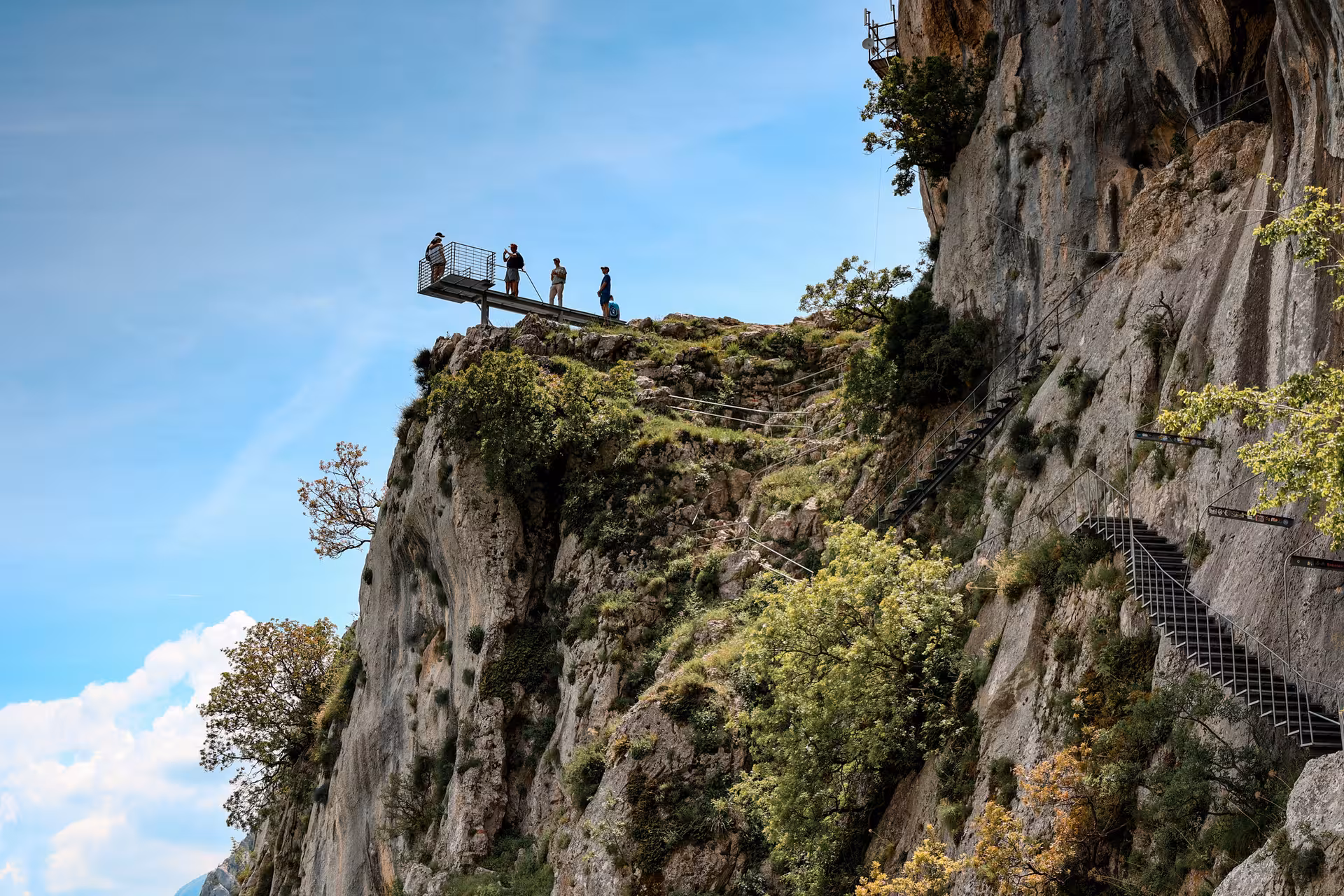Tourists enjoying the panoramic view from an elevated platform at Bovilla Lake, surrounded by rocky cliffs.