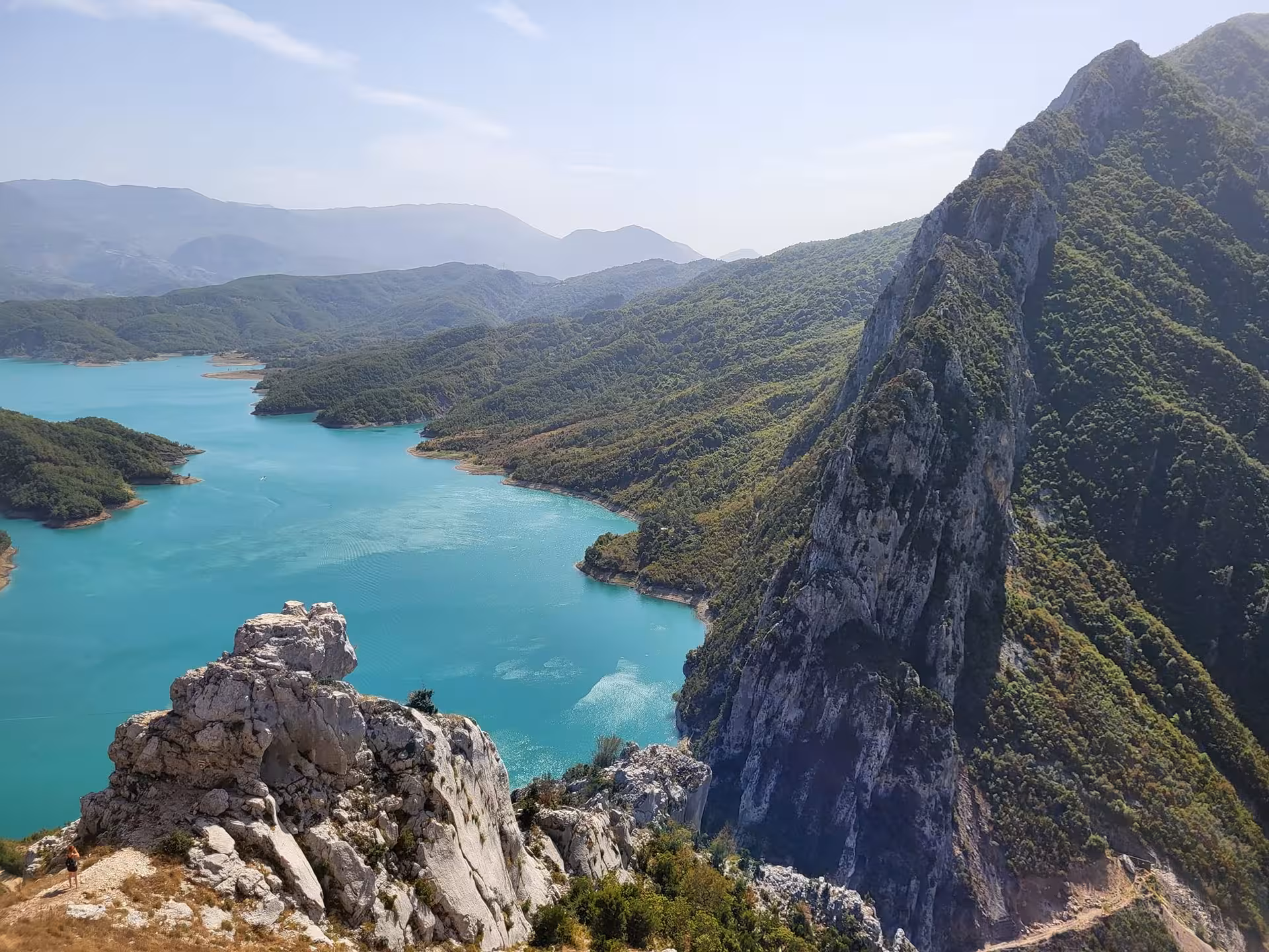 Scenic view of Bovilla Lake with turquoise waters surrounded by lush green mountains and rocky cliffs ideal for day trips.