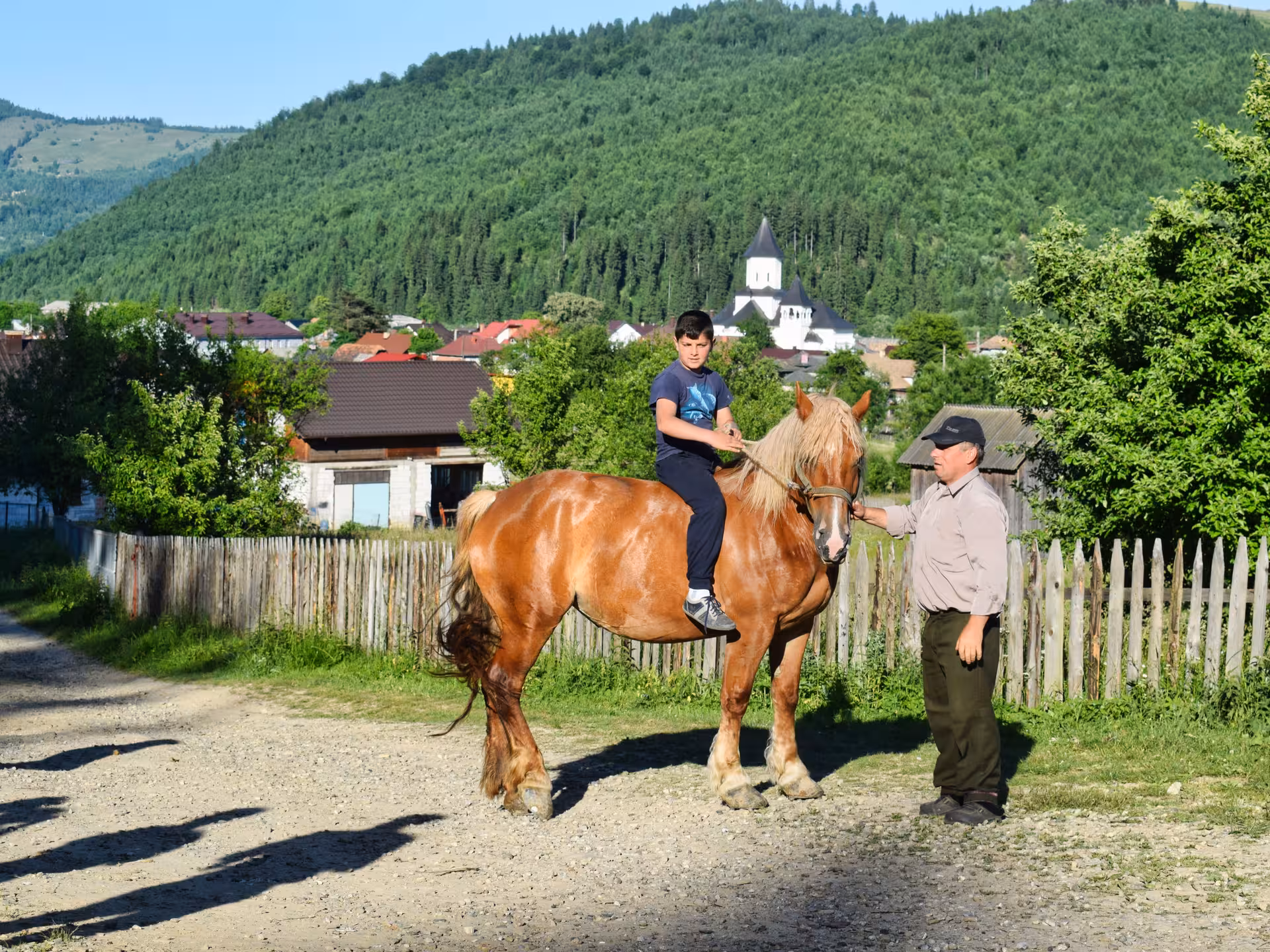 Boy riding a chestnut horse in a Bucovina village with a church backdrop during a 2-day monasteries tour