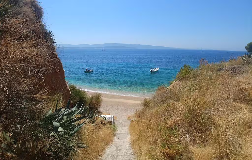 Cliffside path to sandy cove with boats anchored in turquoise sea, peaceful stop on Brac and Solta private tour