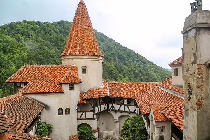 Courtyard and tower of Bran Castle with red-tiled roofs and forested hills in Transylvania, Romania