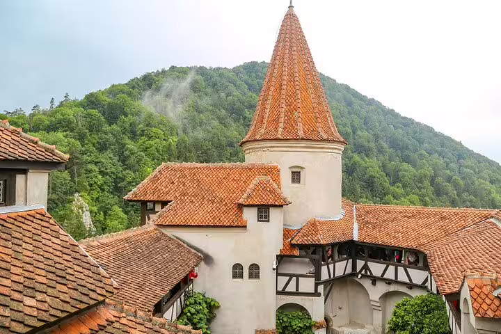 Bran Castle courtyard with orange terracotta rooftops and round tower, surrounded by forested mountains in Transylvania