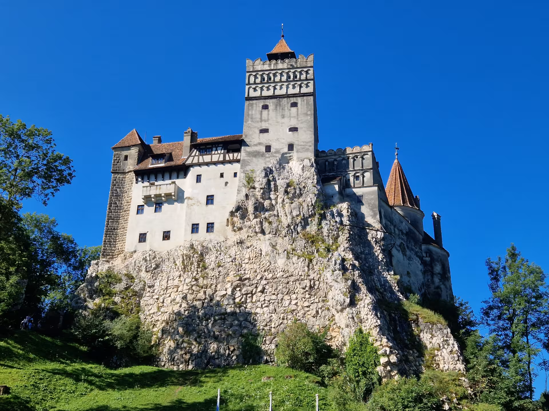 Bran Castle perched on rocky cliff with medieval towers and battlements under blue sky, Transylvania Romania