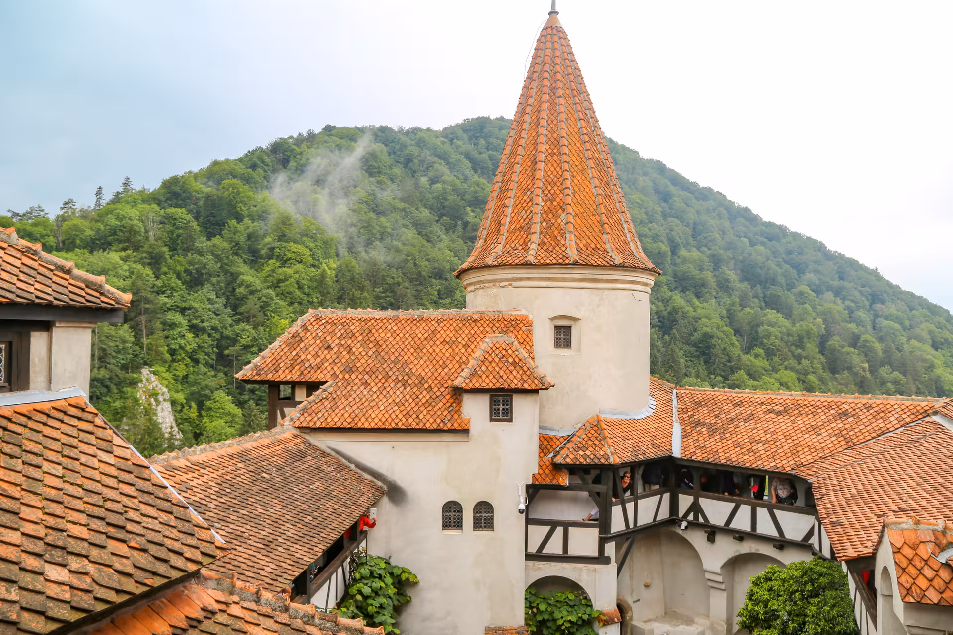 Bran Castle tower with orange terracotta roof tiles surrounded by forested mountains in Transylvania