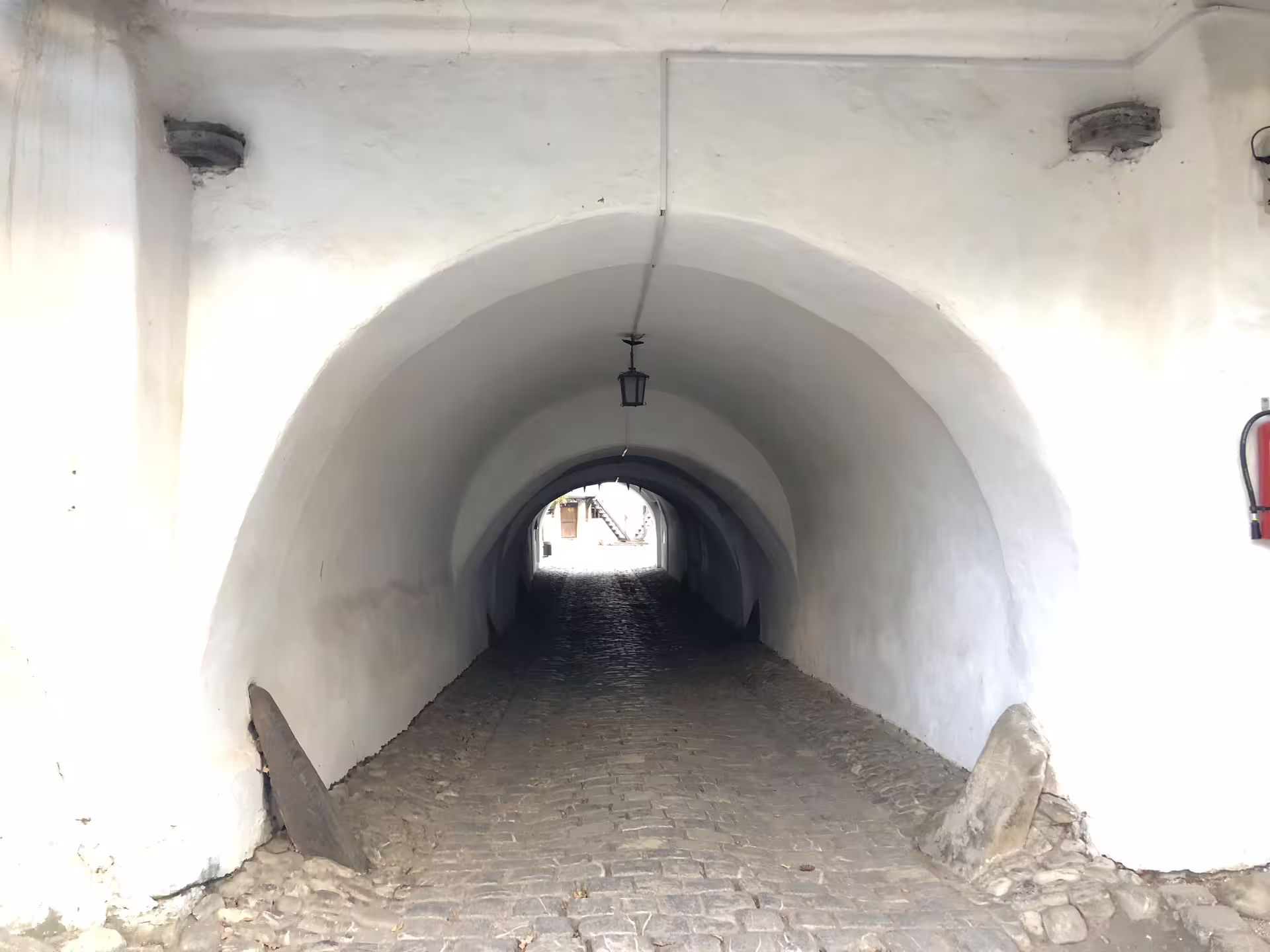 White arched tunnel passageway with cobblestone path leading to a fortified church in Brasov