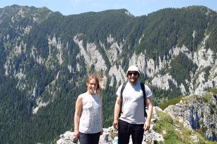 Two hikers posing on a rocky mountain summit with forested peaks near Brasov, Romania
