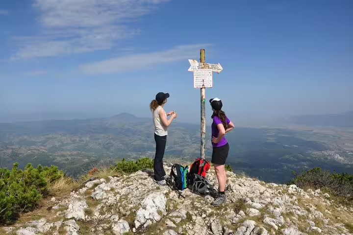 Two hikers at mountain summit trail sign with panoramic valley views during Brasov nature trek