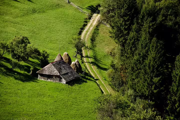 Aerial view of a rustic wooden farmhouse with haystacks on green hillside meadow near Brasov