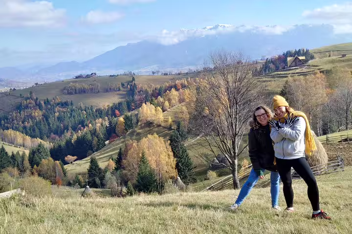 Two women posing on a hillside with colorful autumn forest and snowy Carpathian mountains near Brasov