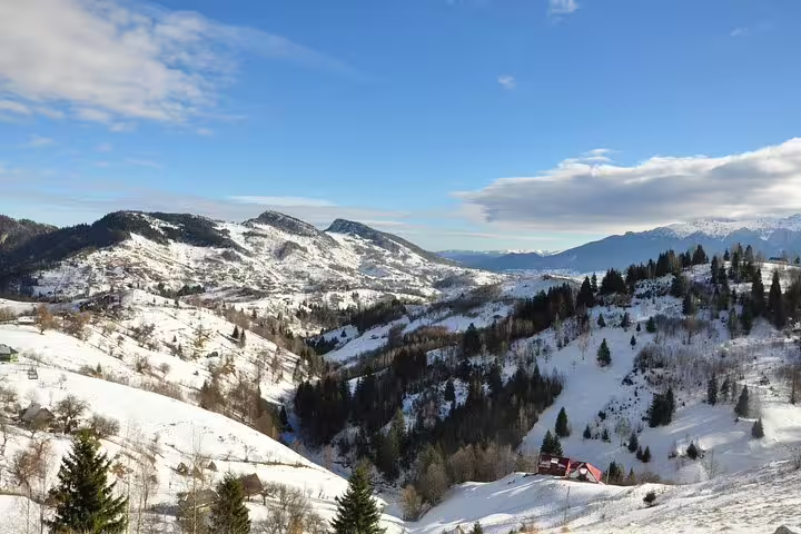 Snow-covered mountain valley with pine forests and scattered buildings near Brasov in winter