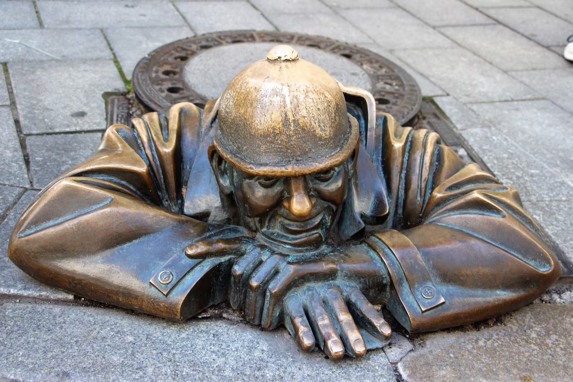 Bronze Cumil statue peeking from manhole in Bratislava historic center, highlight of self-guided audio walk