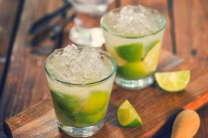 Refreshing Brazilian caipirinhas with lime wedges and crushed ice on a wooden board, perfect for a summer evening.