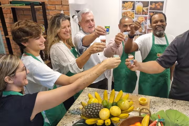 Happy group raising glasses in a Brazilian cocktail workshop, featuring tropical fruits and a cheerful atmosphere.