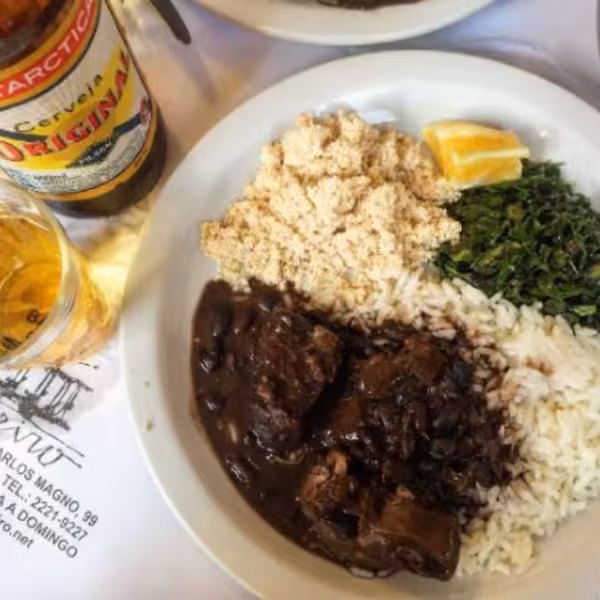 Traditional Brazilian feijoada with rice, greens, and beer, perfect for a culinary tour in Rio de Janeiro.