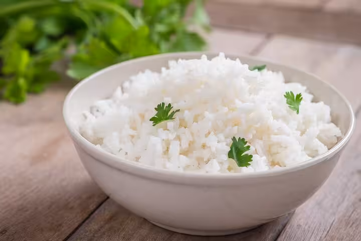 Bowl of fluffy white rice garnished with fresh parsley on a wooden table, highlighting a classic Brazilian side dish.