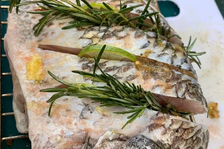 Freshly prepared fish garnished with lime and rosemary, ready for grilling in a Rio seafood cooking class.