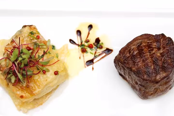 Elegant plating of Brazilian steak with lasagna, garnished with fresh herbs and decorative sauce.