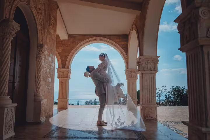 Bride and groom share a joyful moment under an elegant archway overlooking the sea in Ayia Napa.