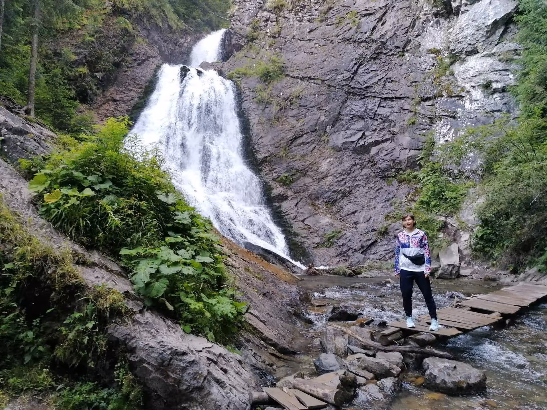 Hiker standing on wooden bridge below Brides Waterfall cascading down rocky cliffs in Apuseni Mountains
