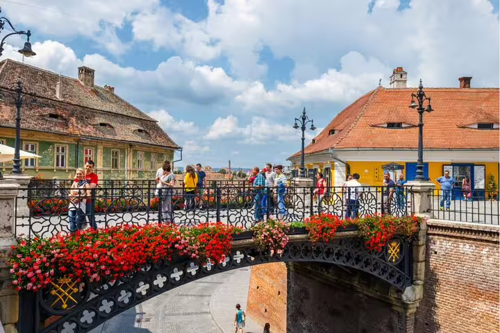 Tourists walking on the ornate Bridge of Lies decorated with red flowers in Sibiu Old Town, Romania