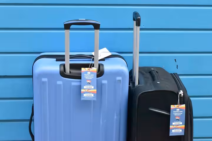 Two suitcases with Stasher tags against blue wall, Brighton luggage storage service for secure short-term bag drop