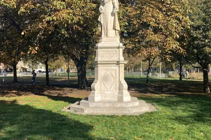 Stone statue pedestal in a sunny Brighton park with autumn trees and green grass