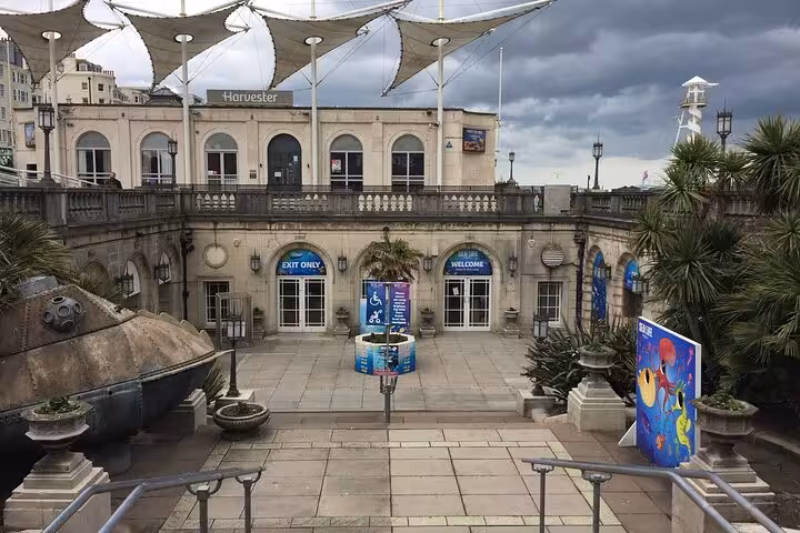 Brighton seafront courtyard with Harvester restaurant, palm trees, and welcome signs on a cloudy day
