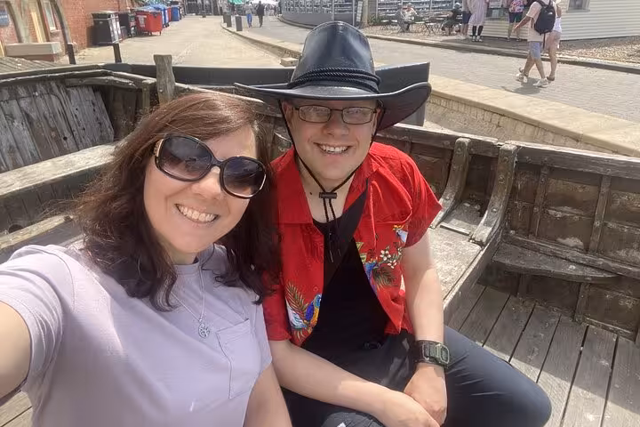 Two smiling visitors sitting on wooden boat structure during Brighton self-guided walking tour on sunny day