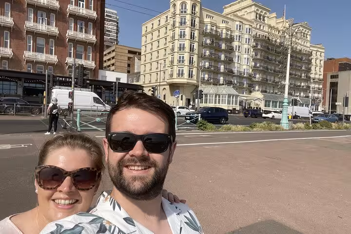 Couple smiling on Brighton seafront with grand Victorian hotel buildings in background on sunny day