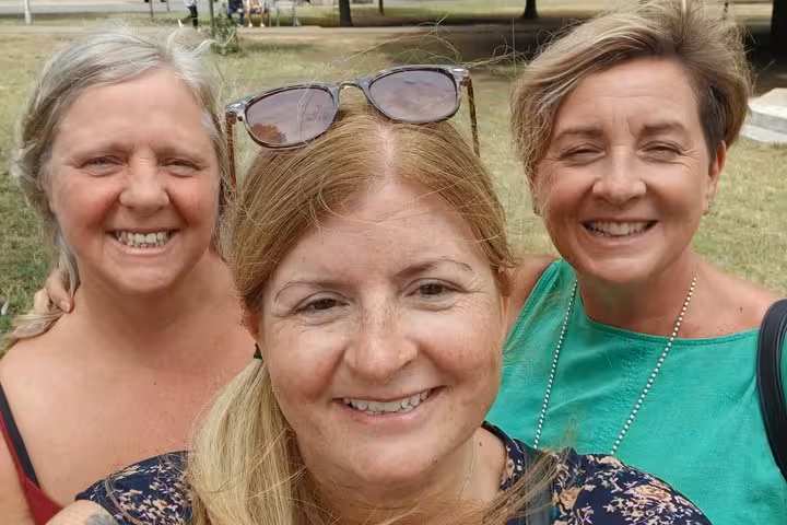 Three smiling women taking a selfie outdoors in a park on a sunny day
