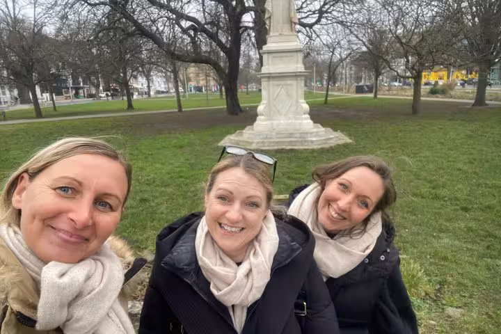 Three women smiling for a selfie near a stone monument in a Brighton park during a walking tour