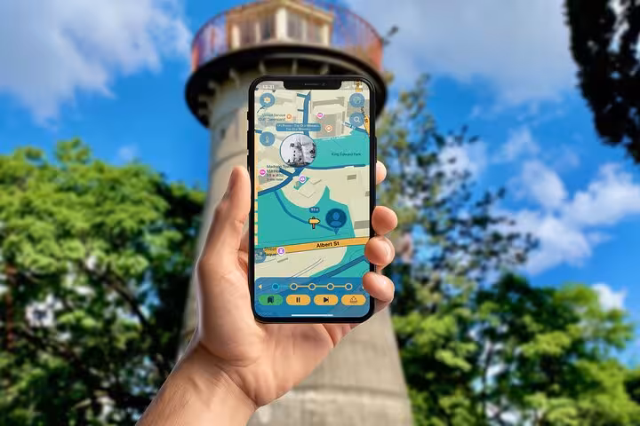 Hand holding smartphone displaying self-guided walking tour map app with historic Brisbane water tower in background